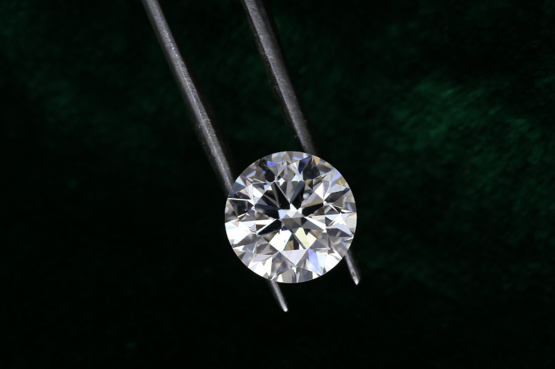 Diamant aus Asche wird von einer Pinzette gehalten zur Größenansicht