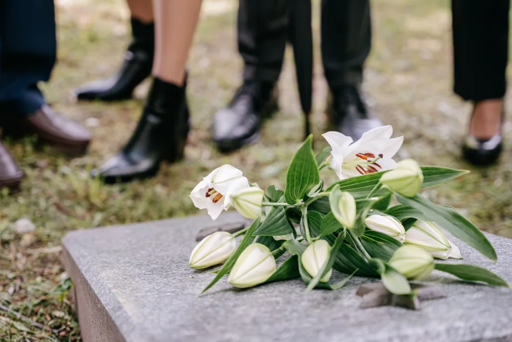Grabschmuck als Zeichen der Anteilnahme Sarg mit Blumen vor einer Gruppe trauernder Personen